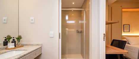 A hotel room with a shower, a bed, a bedside table, and a bathroom with a sink and mirror.