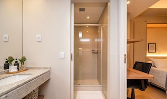 Habitación de hotel con ducha, cama, mesita de noche y baño con lavamanos y espejo.