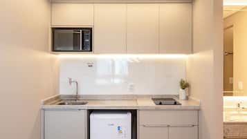 Una cocina compacta con microondas integrado, un lavamanos y un refrigerador pequeño.