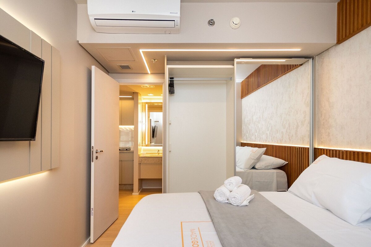 Une chambre d’hôtel équipée d’un lit, d’une télévision, d’un climatiseur, d’un miroir et d’une salle de bain visible à travers une porte ouverte.
