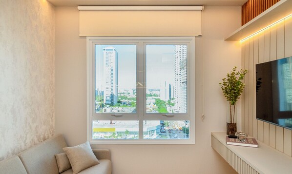 Una sala de estar moderna con un ventanal grande, un sofá, una planta y un televisor de pantalla plana.