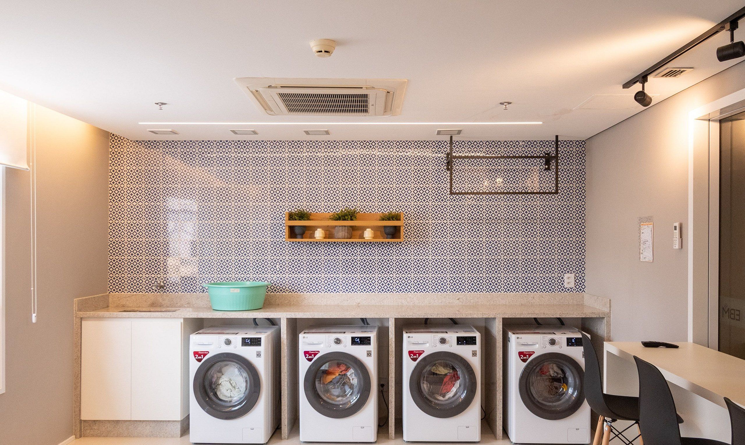 A compact laundry room with four front-loading washing machines, a small shelf with decorative items, and a patterned backsplash.