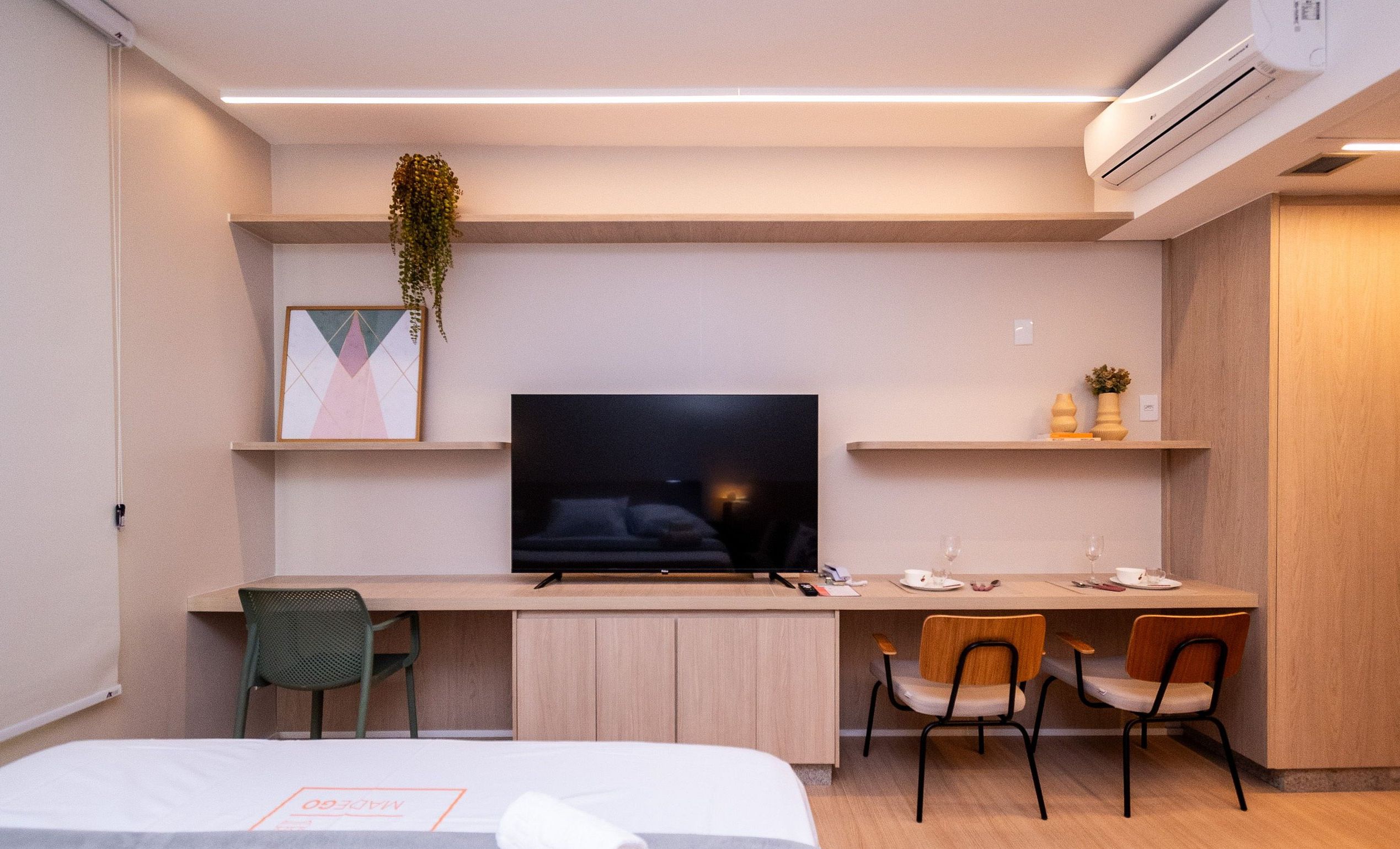Een moderne hotelkamer met een bed, een bureau met een flatscreen televisie, twee stoelen, een tafeltje met een vaas en een hangplant.