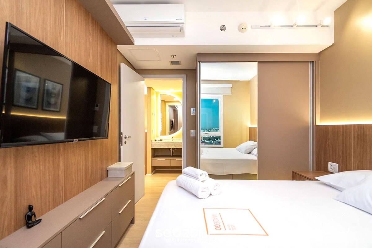 Une chambre d’hôtel dotée d’une télévision à écran plat, d’un lit avec du linge de maison blanc, d’une salle de bain avec un miroir et un lavabo, et offrant une vue sur la ville.