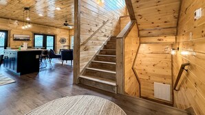 A wooden interior with a staircase, kitchen area, and seating.