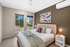 Une chambre dotée d’un grand lit, d’un ventilateur de plafond, d’une fenêtre avec vue et d’un climatiseur fixé au mur.