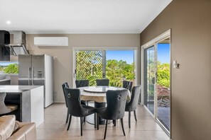 Une cuisine moderne avec un coin repas, une grande fenêtre et une porte-fenêtre coulissante donnant sur un jardin.