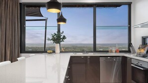 A modern kitchen with a large island, stainless steel appliances, and a view of the landscape through large windows. - On Top of the World S (Anglesea)