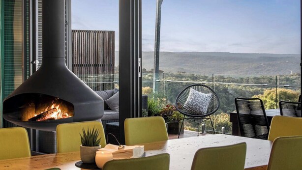 A modern outdoor seating area with a fireplace, green chairs, and a view of the countryside. - On Top of the World S (Anglesea)