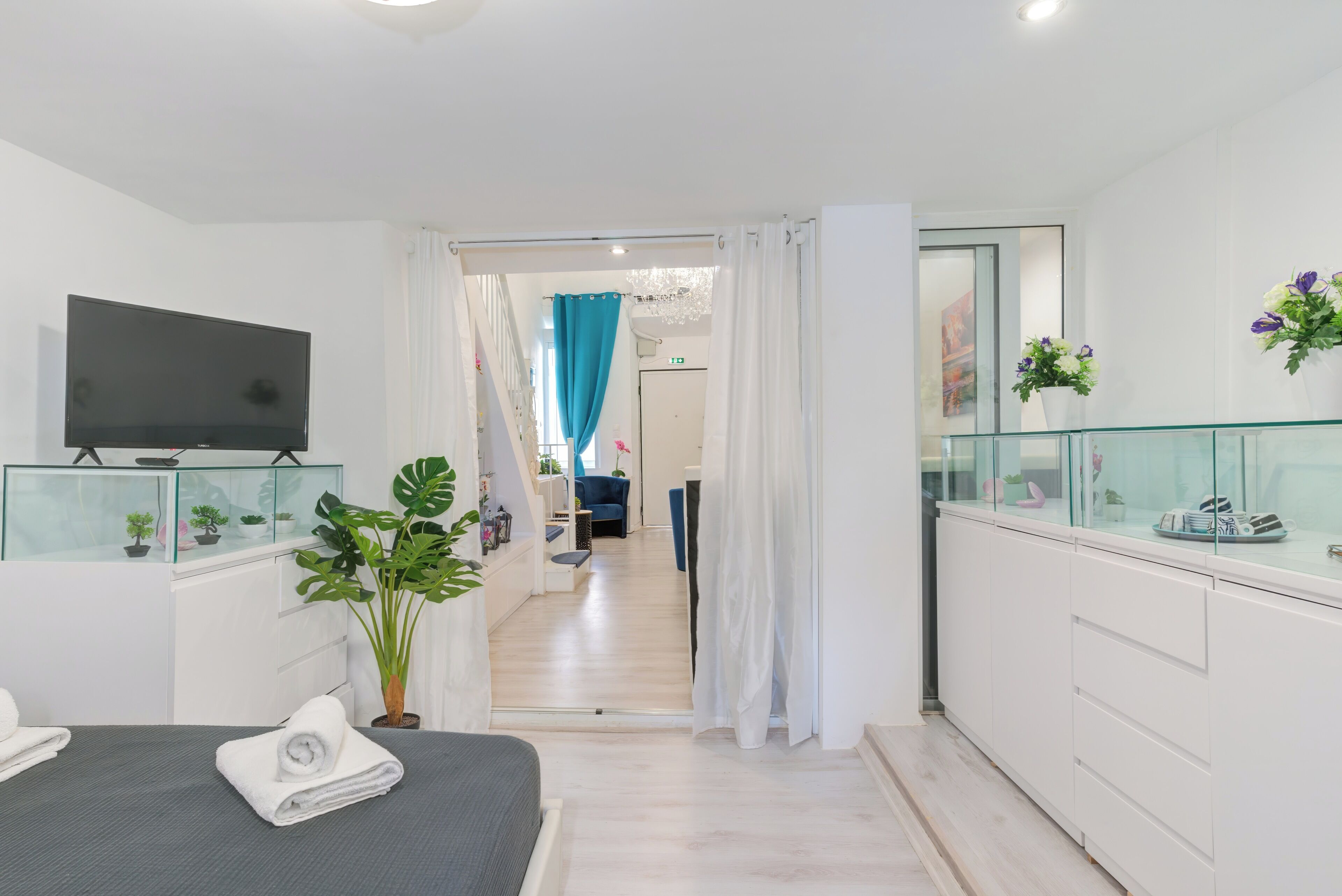 Een hotelkamer met een bed, een televisie, een bureau met een computer, een potplant en een badkamer die door een open deur zichtbaar is.