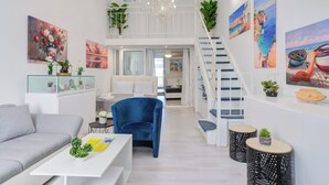 A modern living room with a grey sofa, a blue armchair, and a white coffee table. There is a staircase with a railing leading to an upper level.