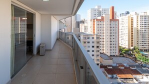 Un balcon avec une porte vitrée, une poubelle et une vue sur des immeubles de grande hauteur.