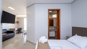 Une chambre d’hôtel avec un lit, un bureau, une chaise, un canapé, une télévision et une salle de bain visible à travers une porte ouverte.