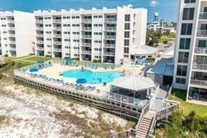 A multi-story hotel with a pool area, outdoor seating, and a beach access deck.