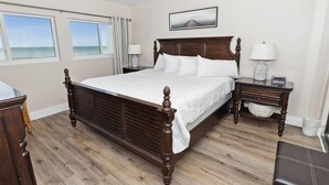A bedroom with a wooden bed, two bedside tables, a nightstand, a window with curtains, and a framed picture on the wall.