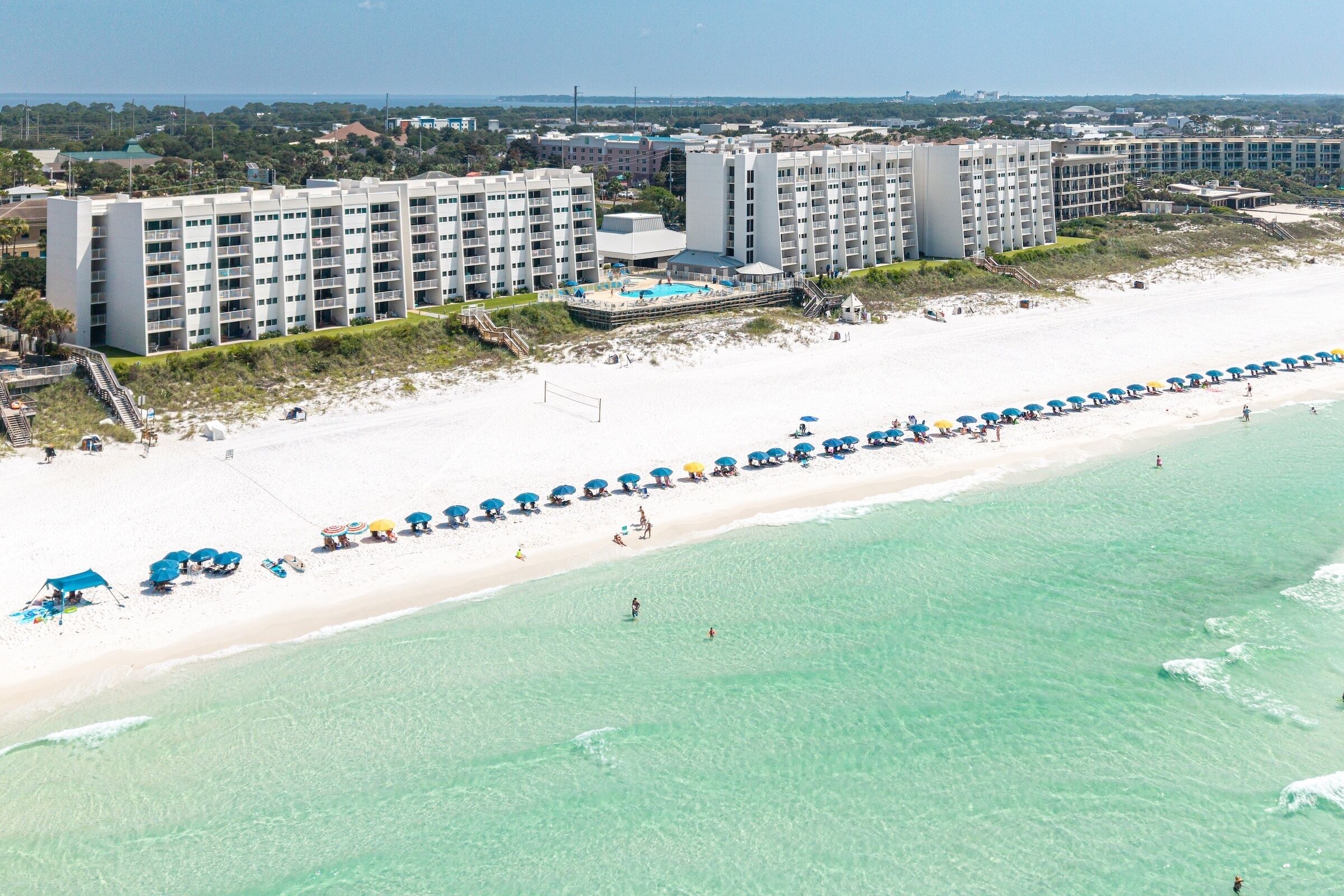 A beachfront hotel with multiple buildings, a sandy beach, and a clear blue sea.