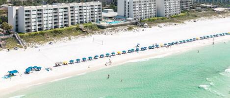 A beachfront hotel with multiple buildings, a sandy beach, and a clear blue sea.