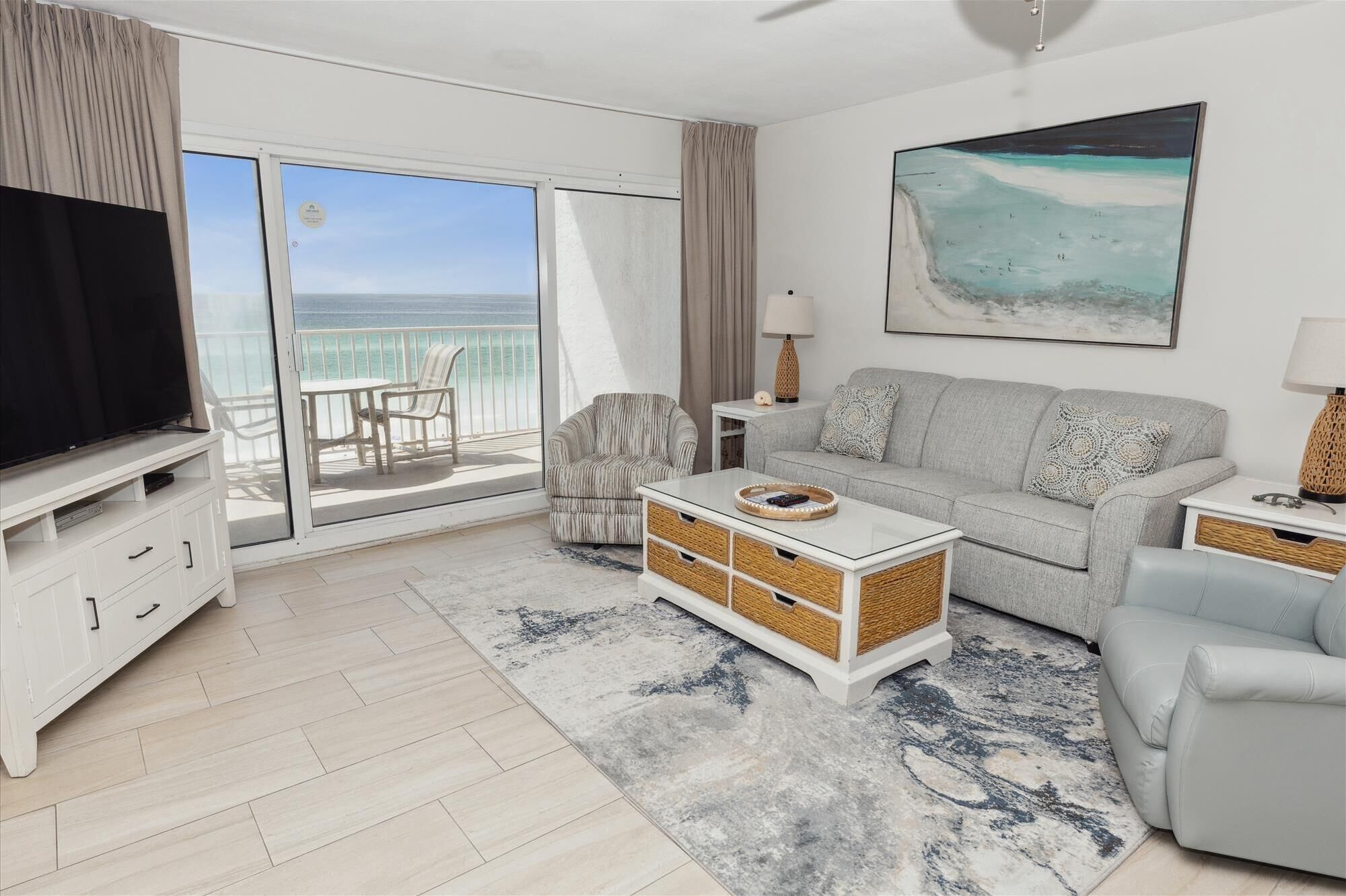 A modern living room with a television, sofa, and a view of the ocean through large sliding doors.