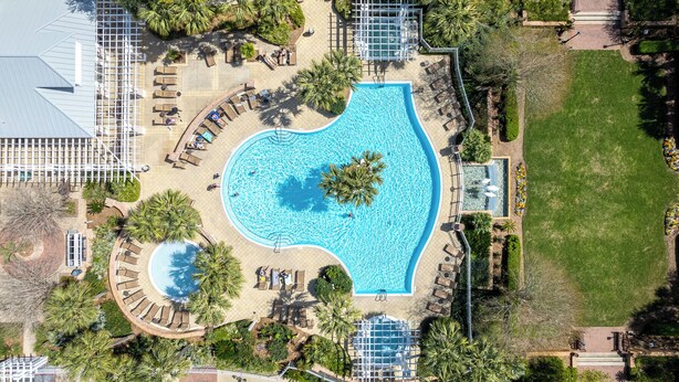 Luchtbeeld van een resort met een groot centraal zwembad, diverse ligbedden en omliggend groen.