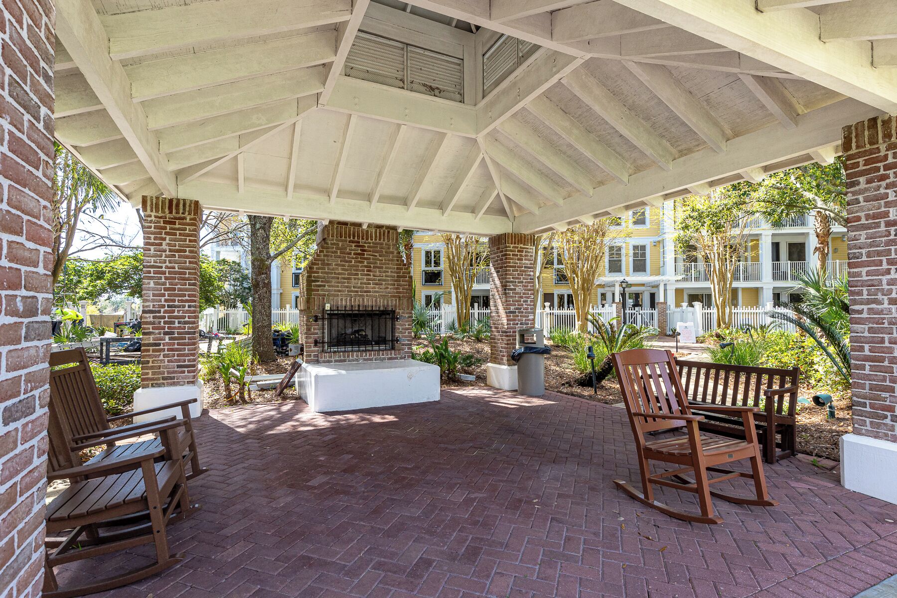 A covered patio with a brick fireplace, two rocking chairs, and a brick floor.