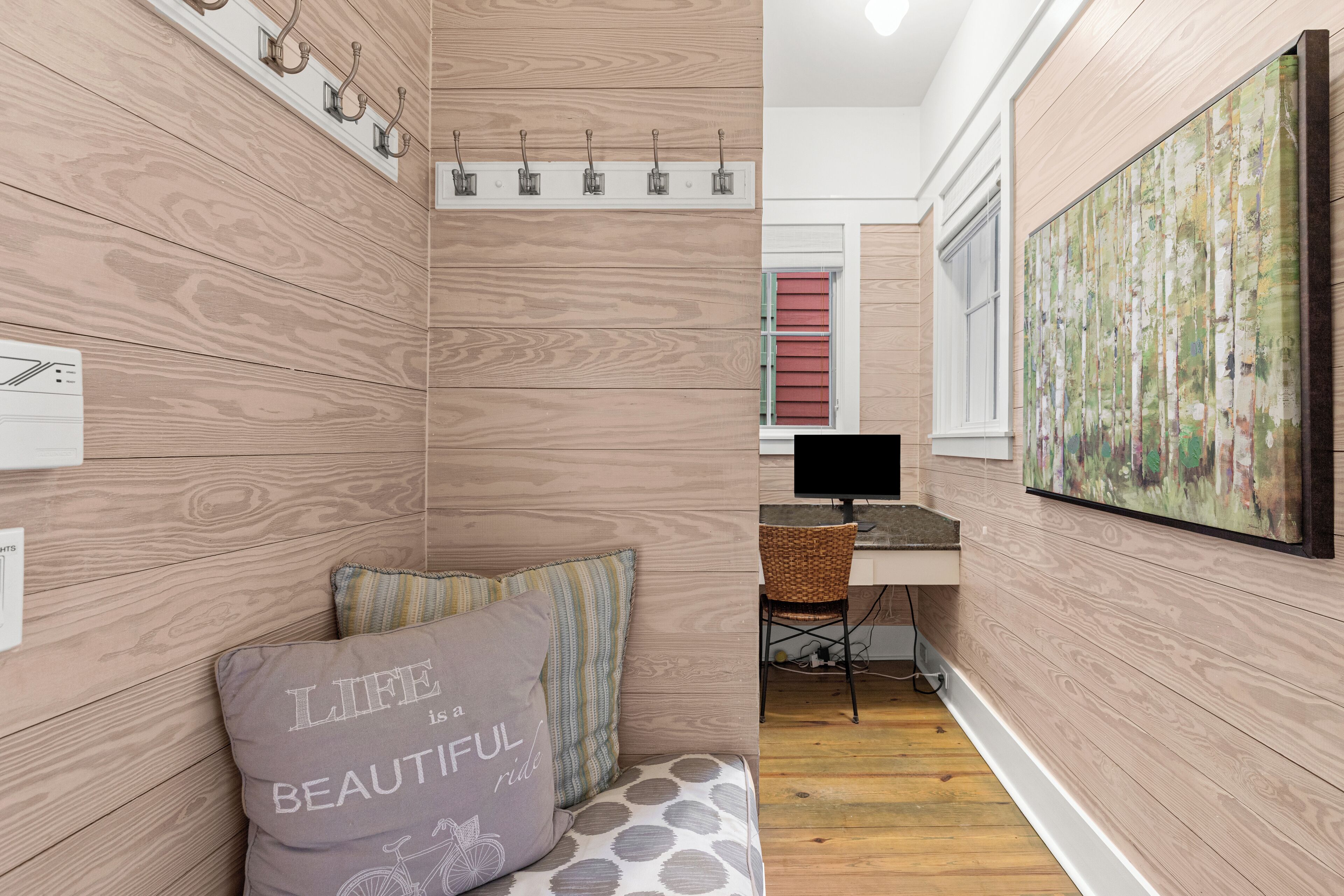 Ein Zimmer mit Holzwandverkleidung, einem Bett mit gemusterten Betttextilien, einem Schreibtisch mit Computer und einem großen, abstrakten Gemälde.