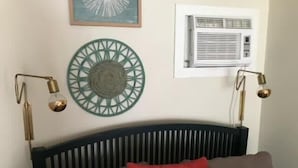 Une chambre à coucher comprenant un lit, un climatiseur fixé au mur, un élément décoratif mural et deux lampes fixées au mur.