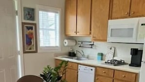 Une cuisine compacte avec des meubles de rangement en bois, un four à micro-ondes, un évier et une petite table à manger avec des chaises.