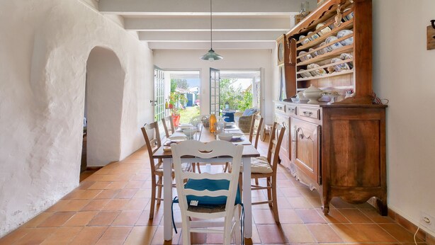 A dining area with a long table, chairs, and a wooden cabinet with shelves. - Loix- Ré Island- House for 5 (Loix)