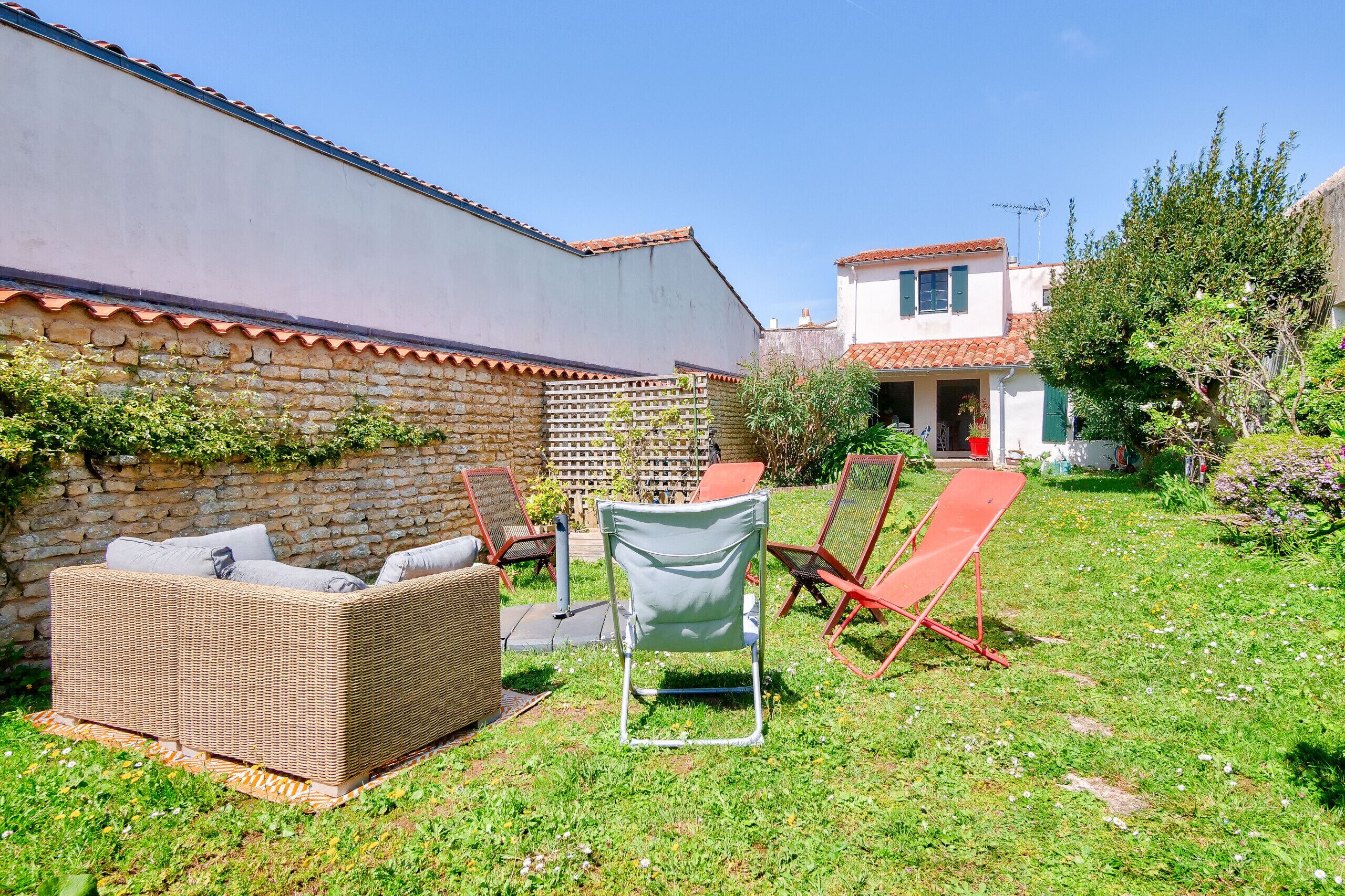 A backyard with a wicker sofa, a green folding chair, and a red lounge chair.