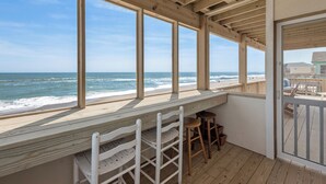 Una terraza de madera con vista al océano, que incluye un banco y taburetes de madera.