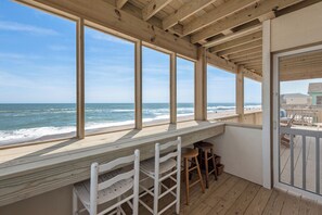 A wooden deck with a view of the ocean, featuring a wooden bench and stools.