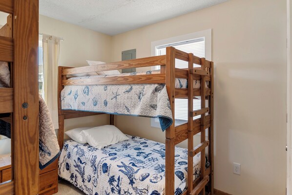 A bunk bed with a blue and white patterned bedspread, a wooden headboard, and a window with blinds. - Everlasting Moon: Oceanfront | Remodeled | Pets OK (Rodanthe)