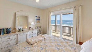 Un dormitorio con cama, cómoda y un amplio ventanal con vistas al océano.