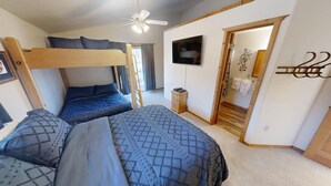 Ein Schlafzimmer mit Etagenbetten, einem Deckenventilator, einem Fernseher und einer Holztür zu einem Badezimmer.