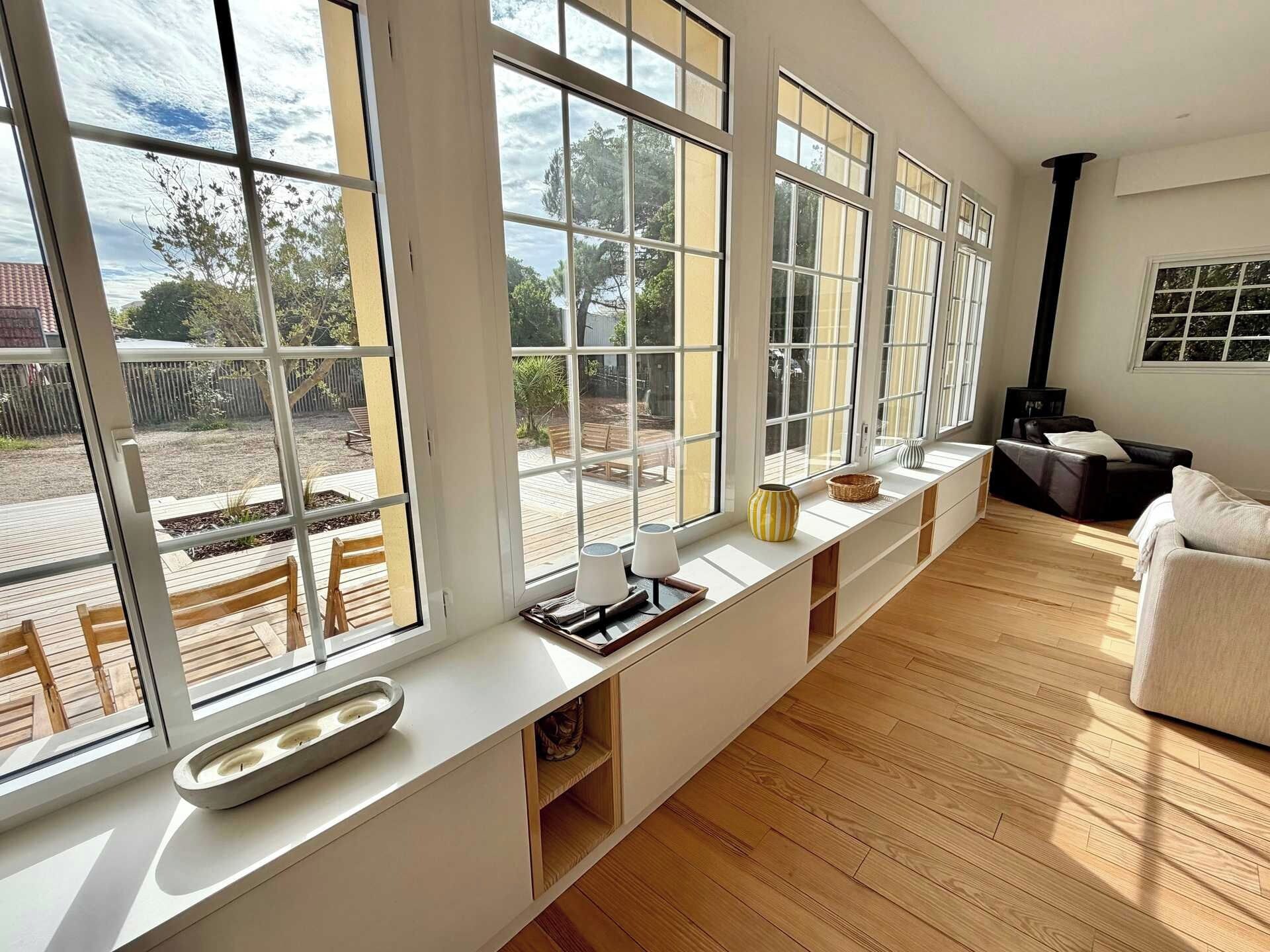 Une pièce spacieuse avec de grandes fenêtres, un plancher en bois et un coin salon agrémenté de coussins.