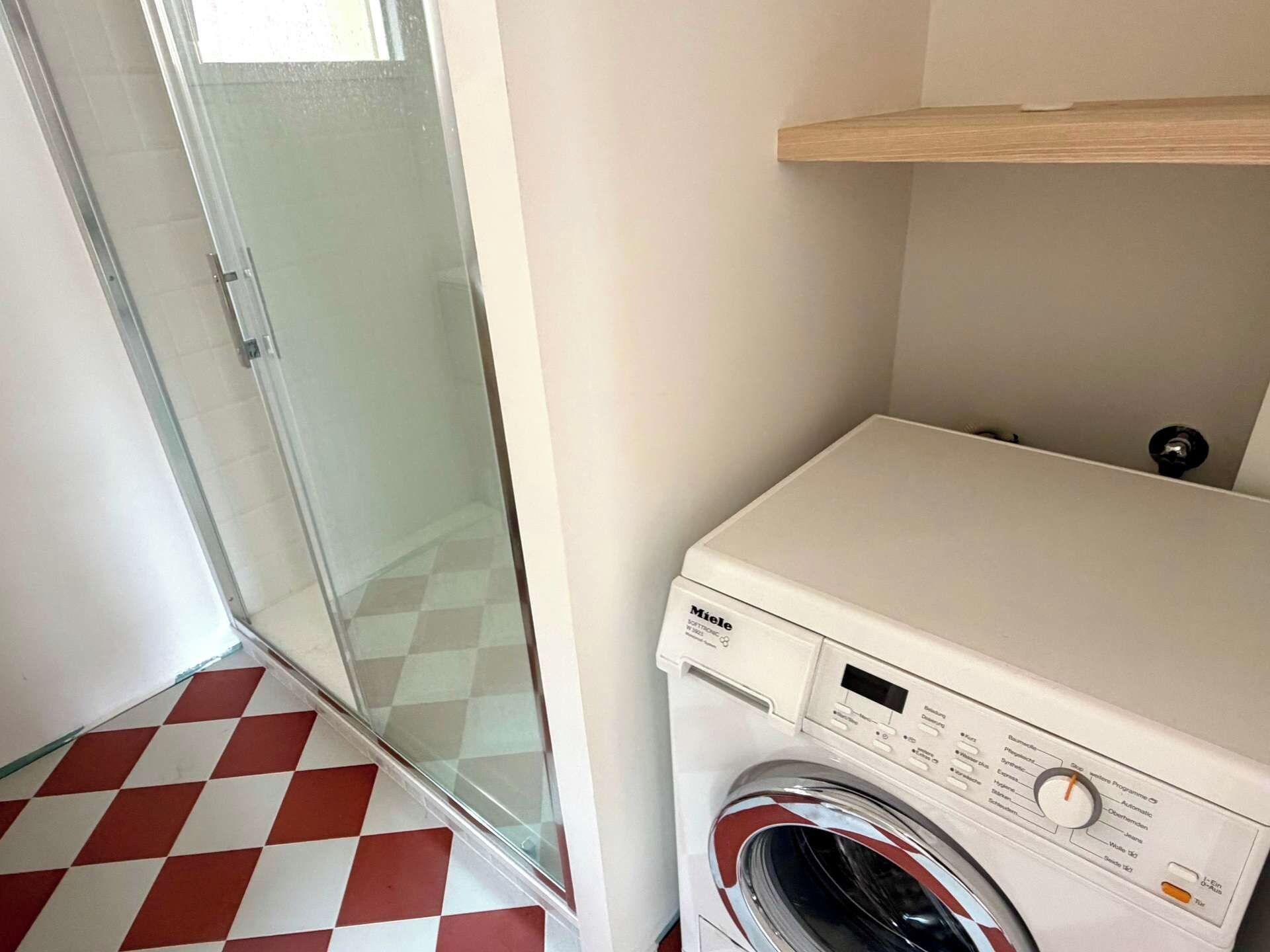 Un cuarto de lavado con lavadora, cabina de ducha de vidrio y piso a cuadros.