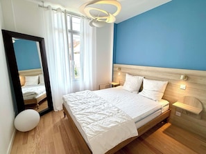 Ein Schlafzimmer mit einem großen Bett, einem Spiegel, einem Fenster mit Vorhängen und einer blauen Wand.