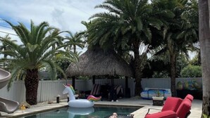 Un espace piscine doté d’un toboggan, de chaises longues et d’une structure recouverte d’un toit de chaume.