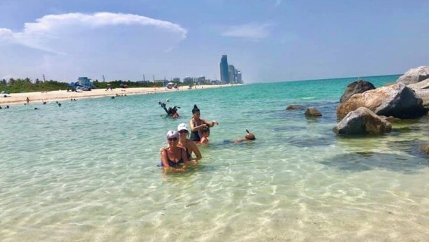 Une plage avec une eau cristalline, des gens qui se baignent et de gros rochers.