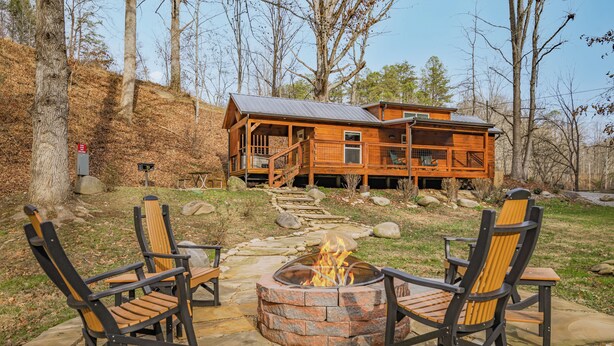 A cabin with a fire pit and rocking chairs in the yard. - Grassy Cove- Cozy Smoky Mtn Cottage w/Hot Tub (Sevierville)