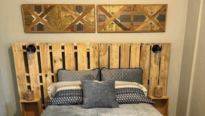 Ein Bett mit einer gesteppten, grauen Bettdecke, einem Holzkopfende mit rustikalem Design und zwei Nachttischen mit Dekoration.