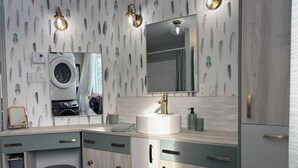 Ein modernes Badezimmer mit einem großen Spiegel, einem runden Waschbecken und einer integrierten Waschmaschine.