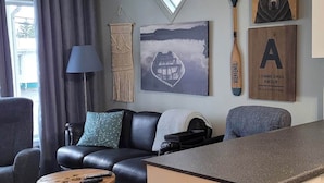 Ein Wohnzimmer mit Sofa, Couchtisch, Teppich und einer Küchenzeile mit Arbeitsplatte und Schränken.