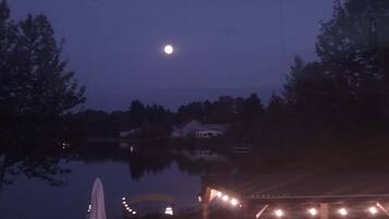 Una vista notturna di una zona sul lago con un gazebo e luci a catena, circondata da alberi e una casa sullo sfondo.