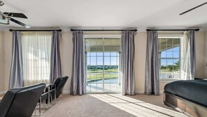 A hotel room with a large sliding glass door leading to a balcony, a bed, a chair, and a ceiling fan.