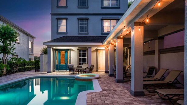 A swimming pool with lounge chairs, a covered patio area, and a building with multiple windows.