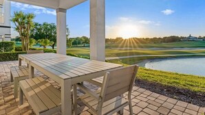 A covered patio with a table and benches overlooking a golf course and a body of water.