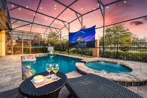 An outdoor pool area with a hot tub, lounge chairs, and a table with drinks.