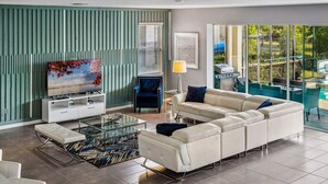 A modern living room with a sofa, TV, and a glass coffee table. - 9BR villa w/ pool, hot tub & patio (Kissimmee)