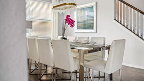 A dining area with a glass-top table, white chairs, and a modern chandelier. - 9BR villa w/ pool, hot tub & patio (Kissimmee)